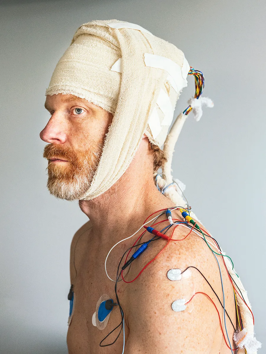 A white man with a bandaged head and wires attached to his upper body for medical monitoring after brain surgery.