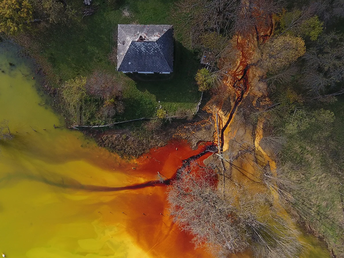 An Aerial shot of a bright yellow and orange body of water by a building on the shoreline. 