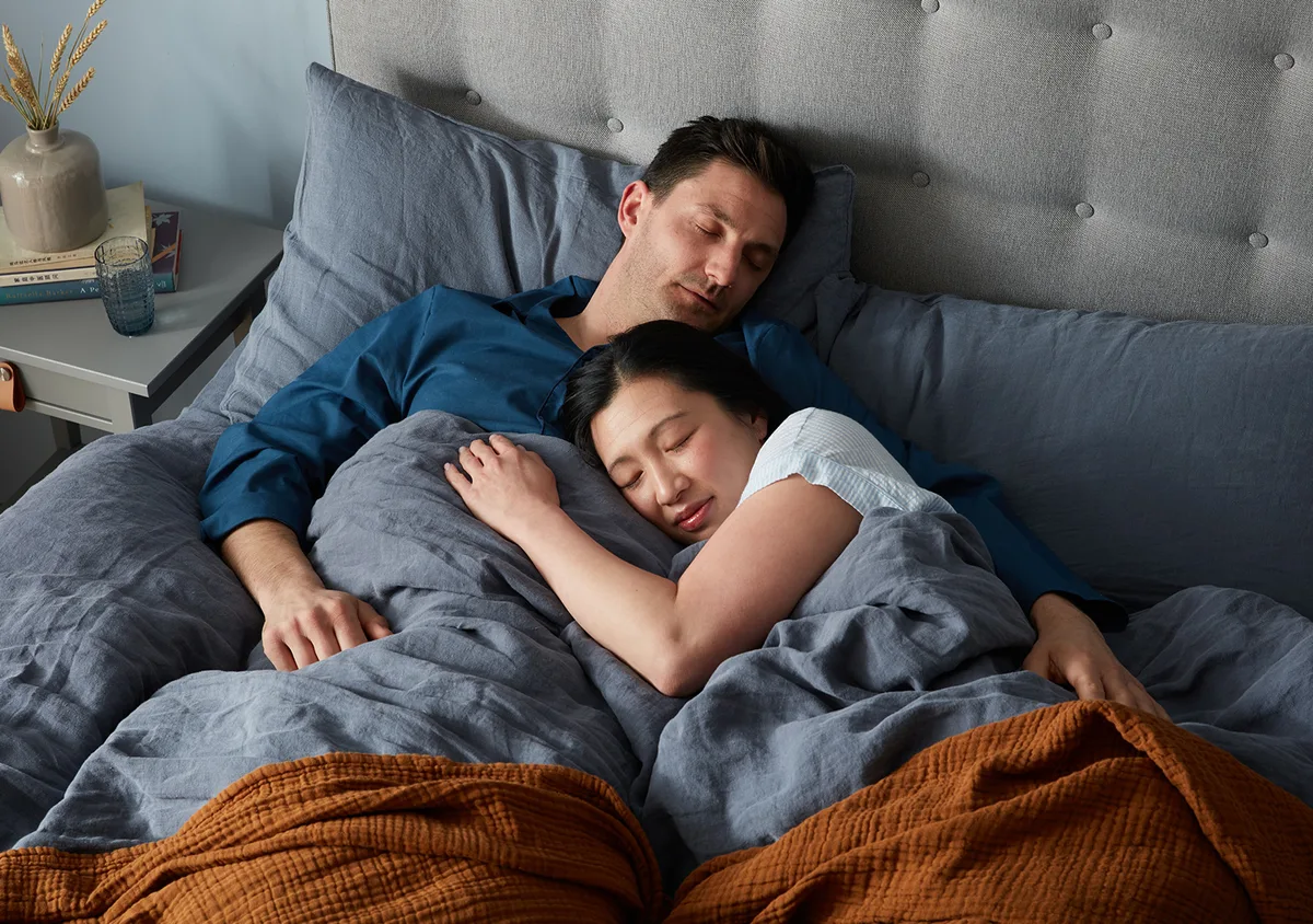 White man and Asian woman cuddling while sleeping in cosy bed