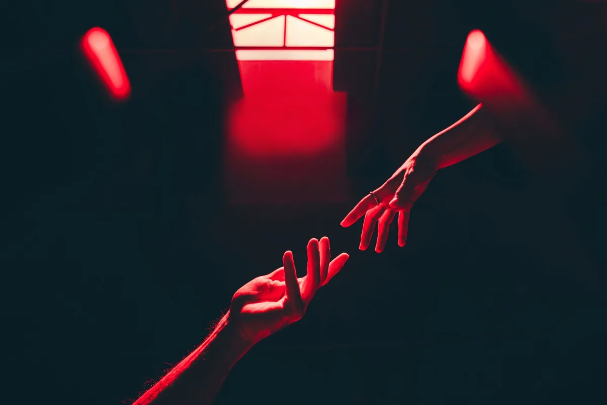Two hands reaching across a room in red light
